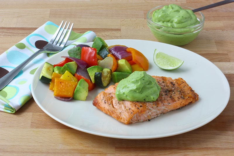 Plate of grilled veggies and salmon topped off with avocado sauce