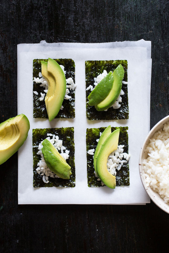 sheets of cut nori topped with rice and avocado slices